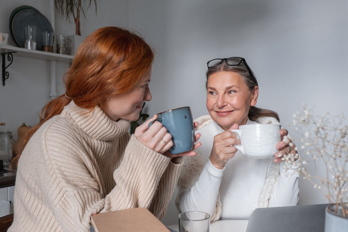 Duas amigas a conversar e a sorrir à mesa, com café.